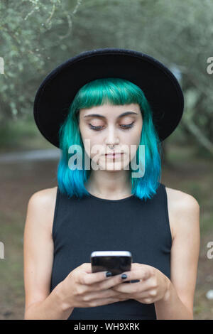Ritratto di giovane donna con tinti di blu e verde per i capelli e piercing per il naso utilizza lo smartphone Foto Stock