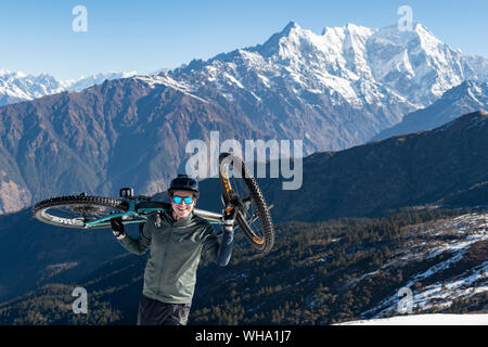 Un mountain biker porta la sua moto fino in Himalaya con vedute della gamma Langtang nella distanza, Nepal, Asia Foto Stock