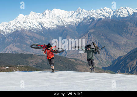 I ciclisti di montagna portano le loro moto fino una coperta di neve pendenza in Himalaya con vedute della gamma Langtang nella distanza, Nepal, Asia Foto Stock