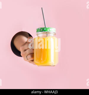 Il succo di arancia in mason jar holding femmina attraverso la mano nel foro. Foto Stock