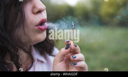 Ragazza di fumare la marijuana medica giunto all'esterno. Le giovani donne di fumare cannabis blunt, close-up. La cannabis è un concetto di medicina di erbe. Foto Stock