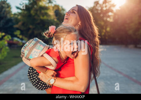 Felice incontro di madre sua figlia dopo aver aperto le classi di scuola primaria e di solletico kid. Famiglia avendo divertimento. Bambino ridere playing game Foto Stock