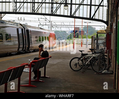 Un treno vergine si erge a Stoke on Trent stazione ferroviaria formando un servizio a Londra Euston come un passeggero in attesa di un altro treno effettua una chiamata telefonica Foto Stock
