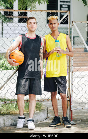 Ritratto a figura intera di gravi giovani ragazzi bello giocare gioco di basket sulla strada corte Foto Stock