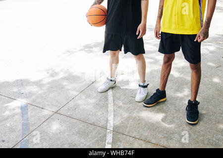 Immagine ritagliata di giocatori di pallacanestro in bianco e nero e giallo permanente uniforme su asfalto tribunale aperto con sfera Foto Stock