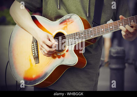 Un ragazzo in una felpa con cappuccio verde svolge un triste melodia con un mediatore su un luminoso chitarra acustica. Foto Stock