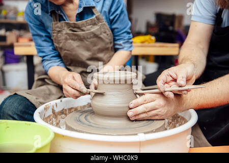 Donna senior di argilla di filatura su una ruota con un aiuto di un insegnante di classe in ceramica Foto Stock