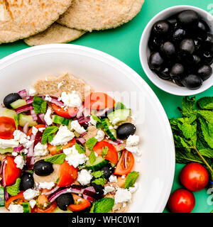 Chunky fresco e salutare insalata greca con pane pitta, olive nere, il formaggio feta, le cipolle rosse e le foglie di menta Foto Stock