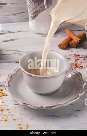 Tradizionale indiano Masala chai tea versare su una bella tazza di ona squallido texture di legno sfondo, vista dall'alto. Ingredienti: cannella, cardamomo, anice, sug Foto Stock