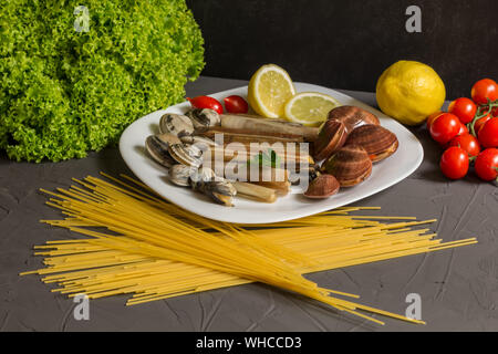 Gli ingredienti freschi per cucinare gli spaghetti e cozze, pomodoro, aglio, prezzemolo su sfondo grigio Foto Stock