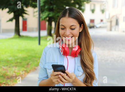 Felice ragazza con smart phone e scegliendo la musica con il suo nuovo mobile app all'esterno. Foto Stock