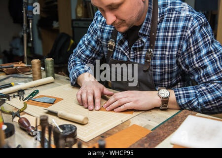 Uomo al lavoro con tessuto in pelle a un workshop. Artigiani in pelle di taglio. Concetto artigianale di produzione artigianale di prodotti in cuoio. Foto Stock