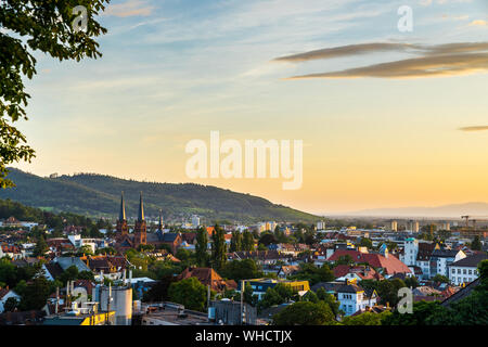 Germania, caldo arancio luce del tramonto sulla skyline della città al di sopra di Freiburg im Breisgau nella foresta nera natura paesaggio che circonda la bella johanneskirche c Foto Stock