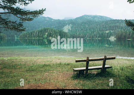 Una panca in legno che si affaccia su un lago chiamato Lago Nero e una foresta in Montenegro. Foto Stock