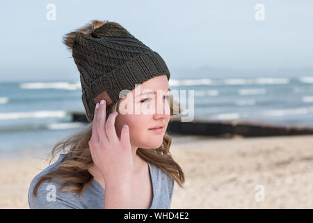Modello femminile indossa maglia verde beanie con altoparlanti Bluetooth interno, ascolto di musica all'aperto. Con le dita sui pulsanti. Foto Stock