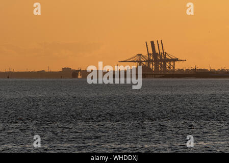 Tramonto dietro Two Tree Island e Canvey Island da Leigh on Sea, Essex con gru portuali DP World London Gateway. Nave portacontainer Foto Stock