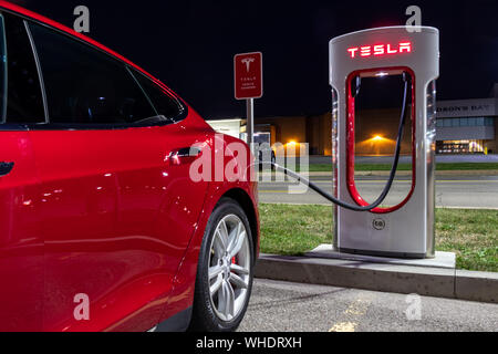 Red Tesla Model S collegata e in carica al Tesla Supercharger di notte. Foto Stock