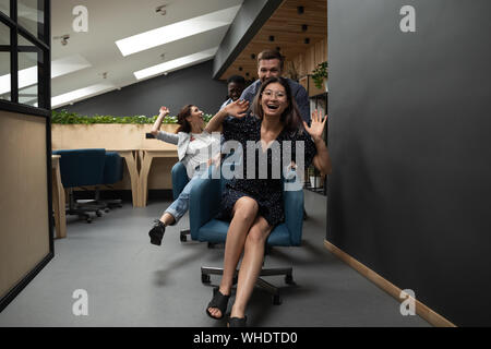 Happy funny diversi colleghi a cavallo su sedie in ufficio moderno Foto Stock