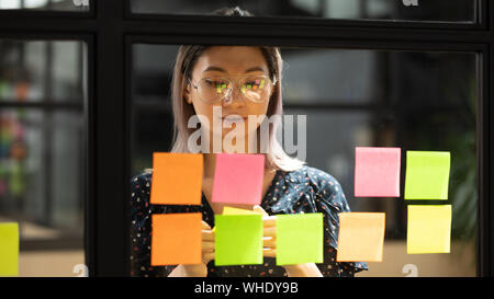 Focalizzato asian coach lavora sul progetto scrivendo su foglietti adesivi Foto Stock