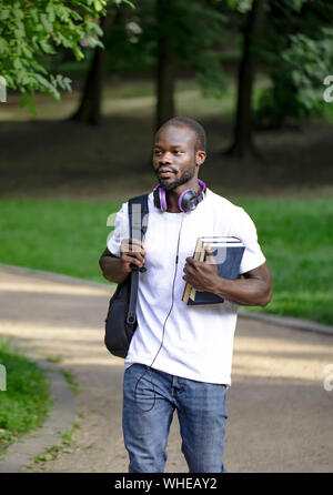 I giovani africani entusiasta studente maschio a piedi attraverso il parco del campus Foto Stock