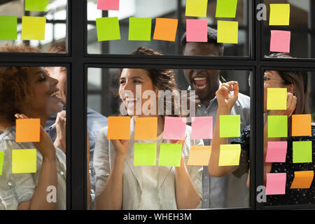 Overjoyed diversi team aziendale di sostare dietro il vetro con note adesive Foto Stock