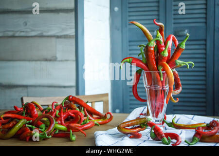 Close up bouquet di lunga peperoncino rosso in un vintage calice di vetro e un mazzetto di peperoncini vicino su una tovaglia naturale, il fuoco selettivo Foto Stock