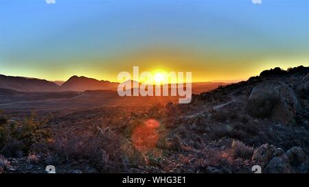 Bel colpo di campo di erba secca e colline con un sole che splende in un cielo blu sullo sfondo Foto Stock
