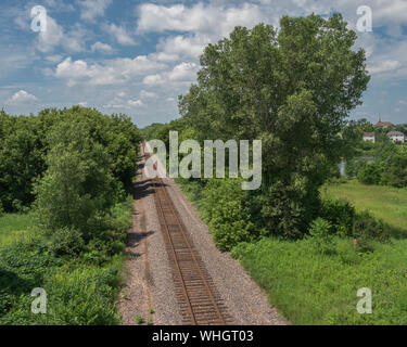 Ferrovia via correndo tra alberi e in fuga la distanza nei pressi di un villaggio come visto dal di sopra su una bella giornata d'estate. Foto Stock