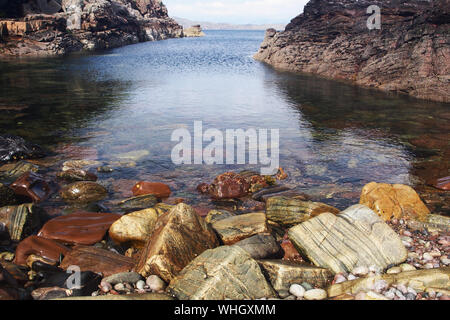 Un basso vista delle rocce colorate a Achnacarnin cove, guardando fuori in mare con il promontorio a fianco sulla penisola Stoer, Sutherland, Scozia Foto Stock