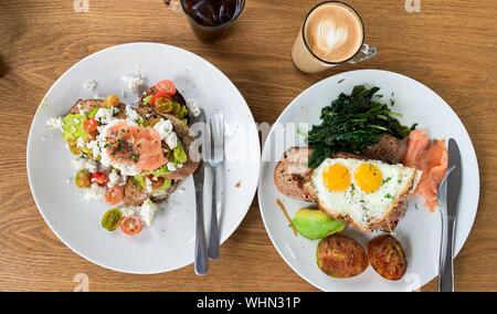 colazione con uova, pesce e verdure su piatti vicino a tazze di caffè e ghiaccio cola Foto Stock