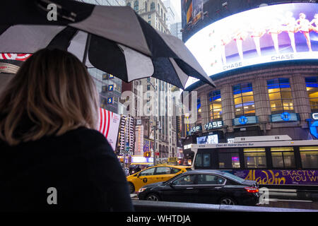 Una donna con un ombrello è attraversare una strada trafficata in Times Square durante un giorno di pioggia. Foto Stock