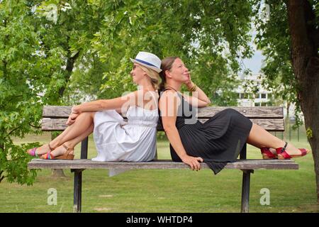 Ritratto di giovane donna in bianco e nero vestito seduto sulla panchina del parco Foto Stock