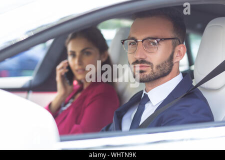 Barbuto marito la guida della vettura mentre la moglie di parlare per telefono Foto Stock