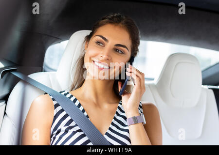 Dark-eyed donna sorridente durante la ricezione della chiamata di telefono da amico Foto Stock