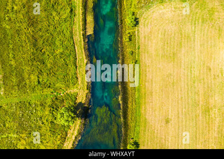 Bellissimo fiume Gacka che scorre tra gli alberi e i campi, summer view, Lika regione della Croazia, drone volando sopra la superficie del fiume Foto Stock