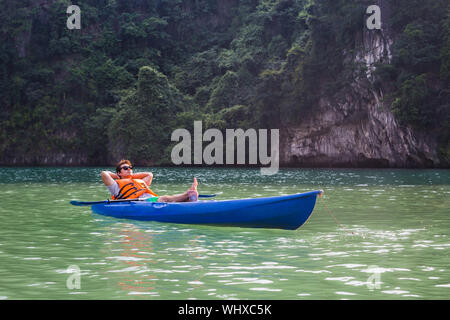 Il Vietnam, baia di Halong kayaking sul sereno l'acqua. Uomo seduto in un kayak di indossare un giubbotto di sicurezza. Foto Stock