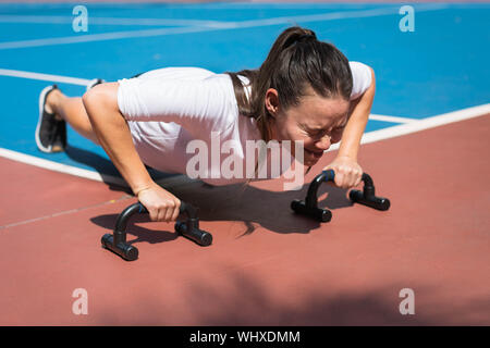 Donna che esercitano su di un campo da tennis all'aperto. Utilizzando le maniglie spinta in su. Foto Stock