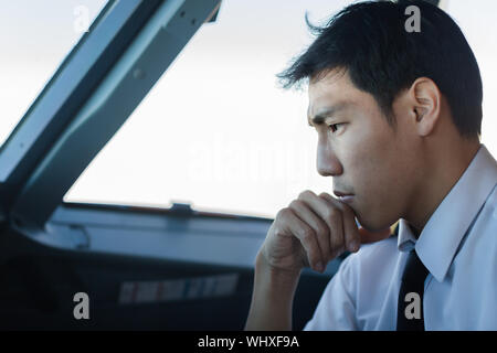 Lato ritratto di un pilota asiatici pensando a un problema di aeromobili Foto Stock
