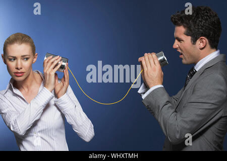 Imprenditore a urlare contro collega femmina attraverso lo stagno può telefono contro sfondo blu Foto Stock