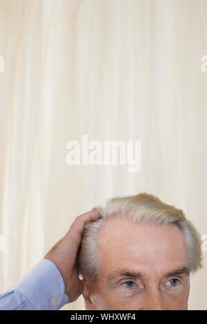 Vista dettagliata sezione alta di un uomo anziano con le mani nei capelli contro la tenda Foto Stock