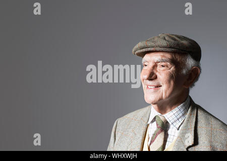 Senior sorridente imprenditore nel tappo piatto contro uno sfondo grigio Foto Stock