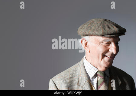 Senior sorridente imprenditore nel tappo piatto contro uno sfondo grigio Foto Stock