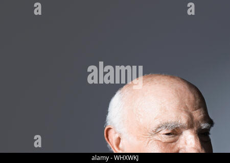 Primo piano di una balding senior uomo contro uno sfondo grigio Foto Stock