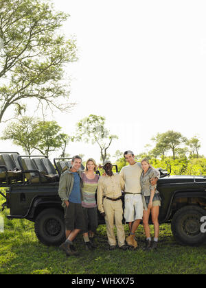 A piena lunghezza Ritratto di gruppo di quattro turisti e guida safari in piedi contro la jeep Foto Stock