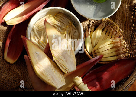 Vista superiore preparare gli ingredienti per alimenti vegani da banana flower, donna mano prendere giovani banane, imbevuto in acqua di limone, blossom fare molti piatti vegetariani Foto Stock