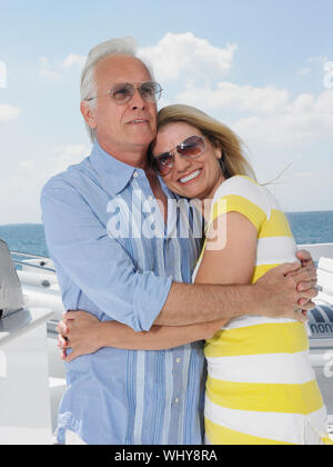 Felice Coppia di mezza età con occhiali da sole mentre abbracciando su yacht Foto Stock