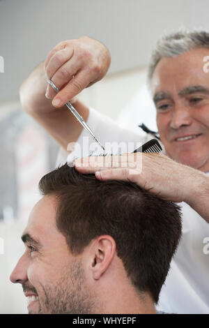 Primo piano di uomo felice di ottenere un taglio di capelli da un barbiere nel salone di parrucchiere Foto Stock