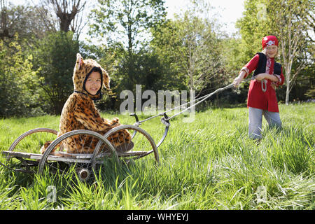 Giovane ragazzo in costume pirata tirando il ragazzo sorridente in jaguar costume sul carrello in giardino Foto Stock