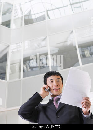 Imprenditore utilizzando il telefono cellulare in atrium di edificio per uffici Foto Stock