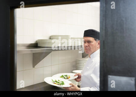 Ritratto di un maschio di chef holding piastre di cibo in cucina Foto Stock